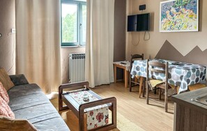 Una habitación acogedora con sofá, una mesa de comedor con sillas, un televisor en la pared y un radiador.
