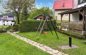 Un jardín con un columpio, un sendero de piedra y una estructura de madera con techo rojo.