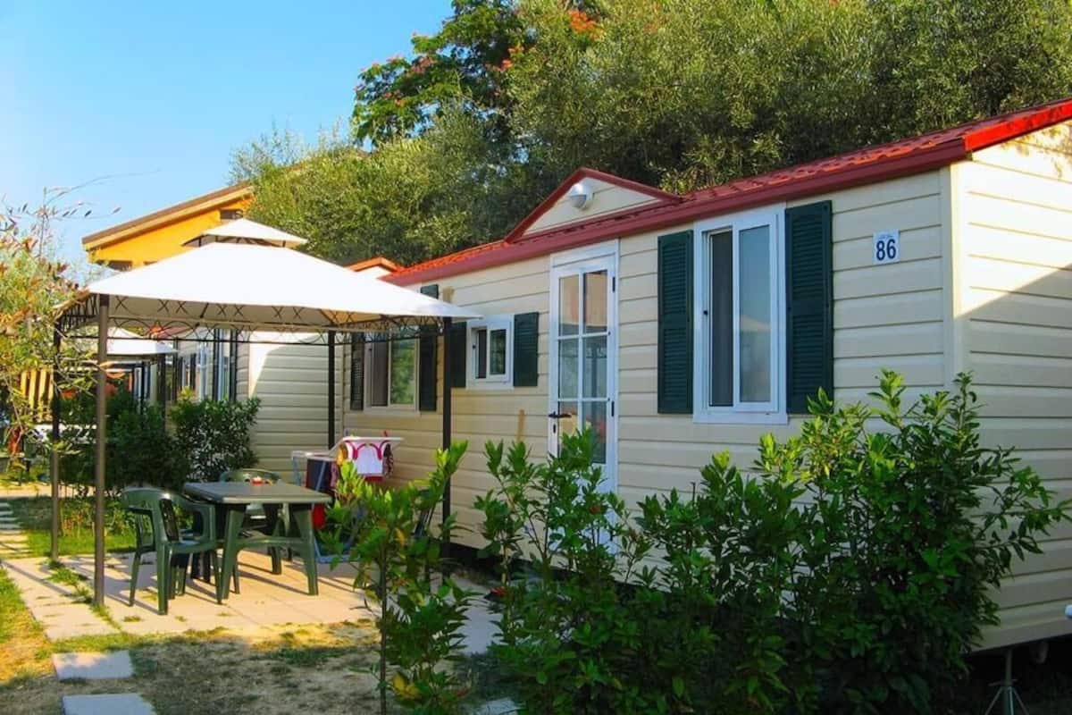 A mobile home with a number '86' on the side, a patio with a table and chairs, and a covered area with an umbrella.