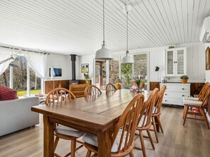 A spacious dining area with a wooden table and chairs, a sofa, and a large window offering a view of the outdoors. - 6 Person Holiday Home in Farso (Farso)