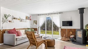 Una sala moderna con sofá, sillón de madera, televisor, chimenea y ventanas amplias.