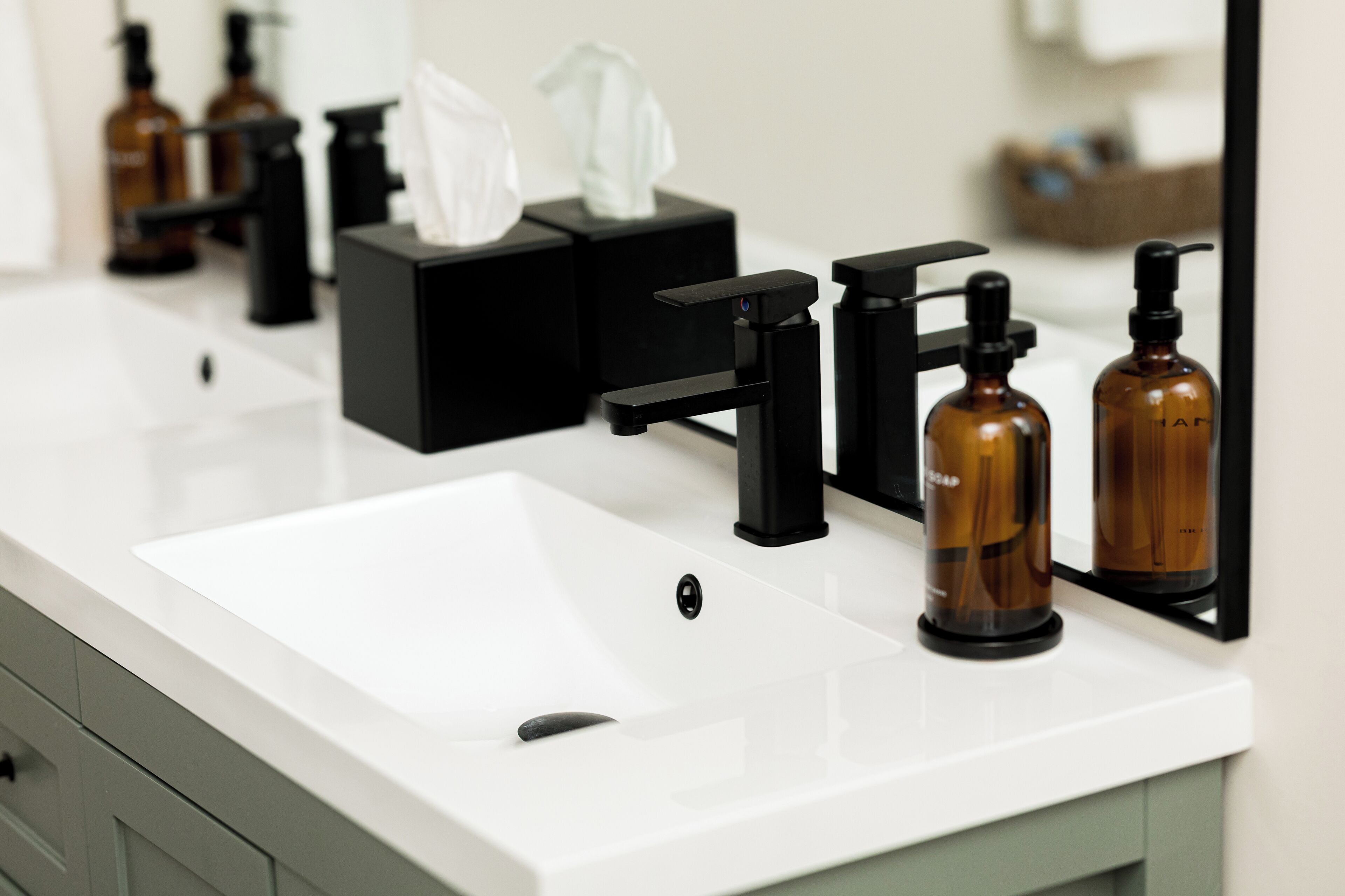 Une salle de bain avec un lavabo blanc, un robinet noir et deux bouteilles marron posées sur le comptoir.