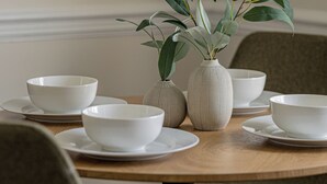Une table à manger avec des bols et des vases blancs, entourée de chaises.