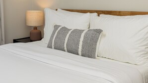 Un lit bien fait, avec du linge de lit blanc et deux oreillers, dont l’un est à rayures.
