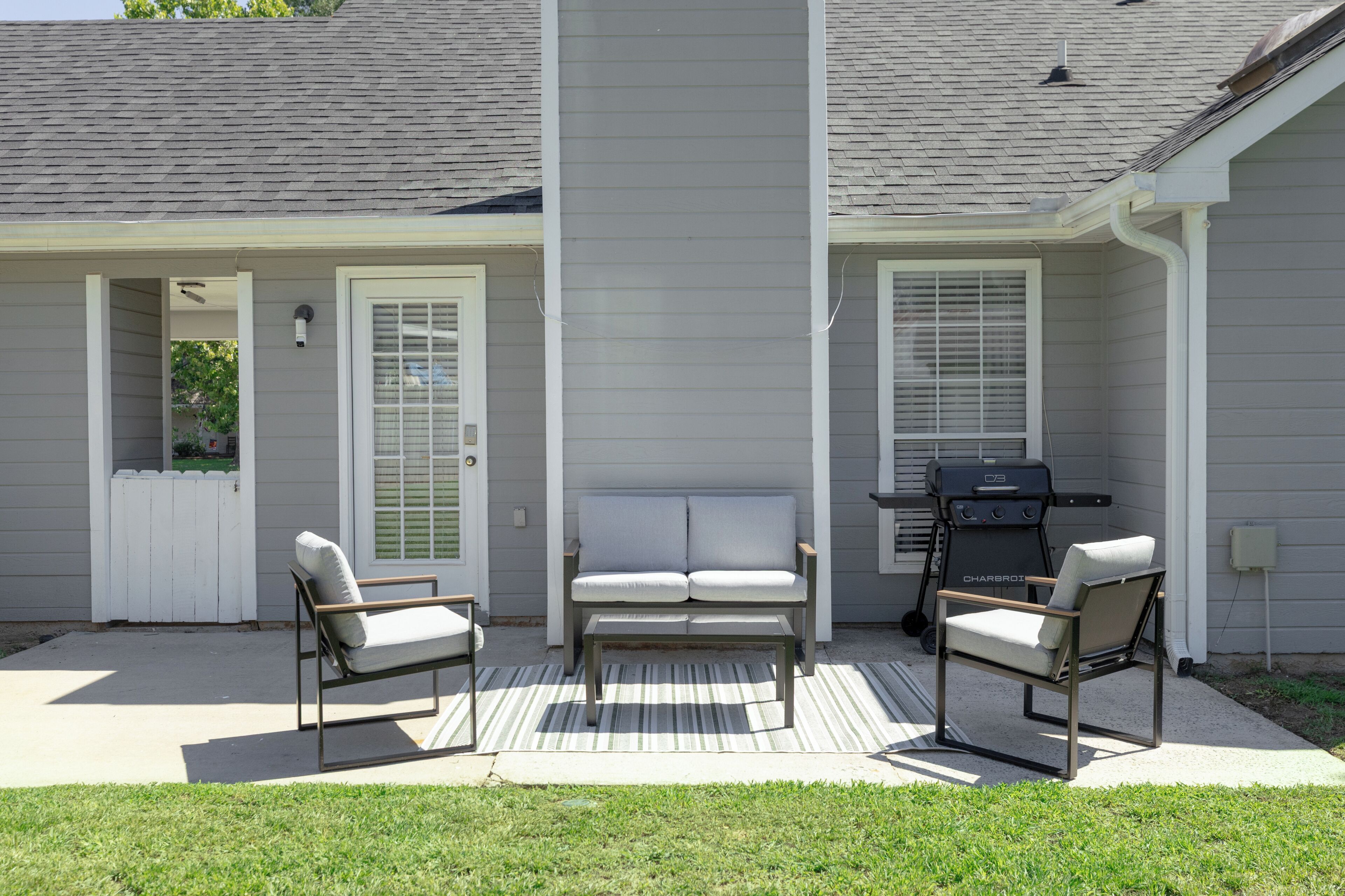 A patio with two chairs, a bench, and a grill.