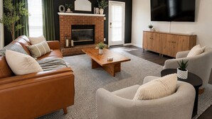 Un salon avec une cheminée, un canapé, un fauteuil, une table basse et un téléviseur fixé au mur.