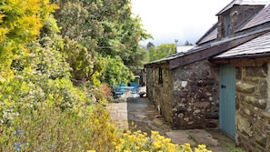 A stone building with a blue door, surrounded by lush greenery and a stone pathway. - Y Cwtch (Dolgellau)