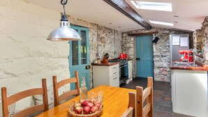 Een rustieke keuken met stenen muren, een houten eettafel met stoelen, een hanglamp en een klein kookeiland met een spoelbak.