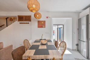 A dining area with a wooden table, chairs, a bowl, and hanging wicker lamps.