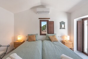 A bedroom with two beds, a window, an air conditioner, a mirror, and bedside lamps.