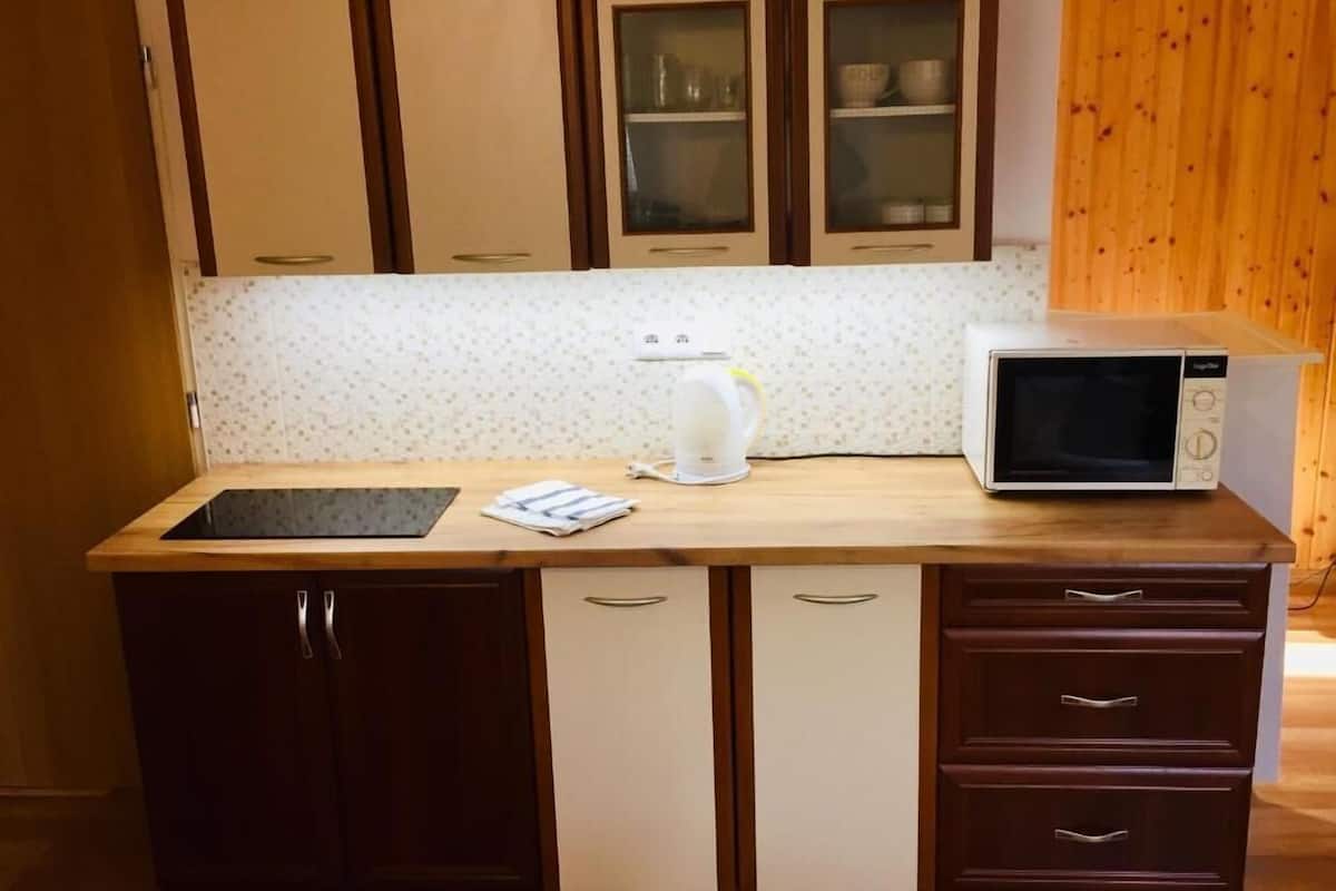 A kitchen with a microwave, a kettle, and a small sink. There are wooden cabinets and a countertop.