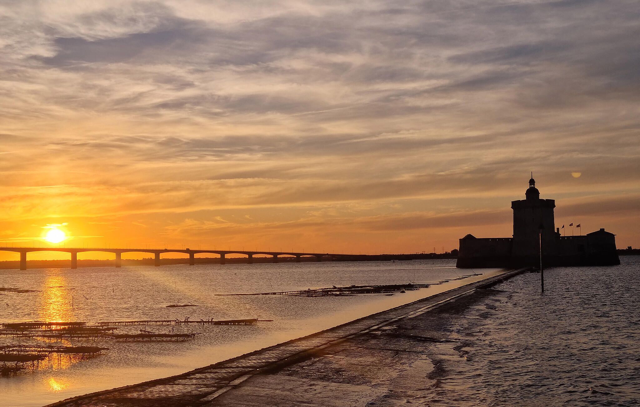 Un coucher de soleil sur une rivière, avec un pont et une tour.