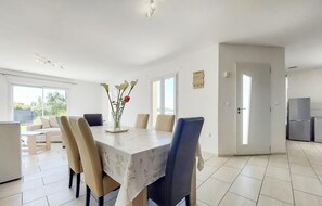 Ein Essbereich mit Tisch, Stühlen und einer Vase mit Blumen. Es gibt eine Küchenzeile mit einem Kühlschrank und einer Tür zu einem anderen Raum.