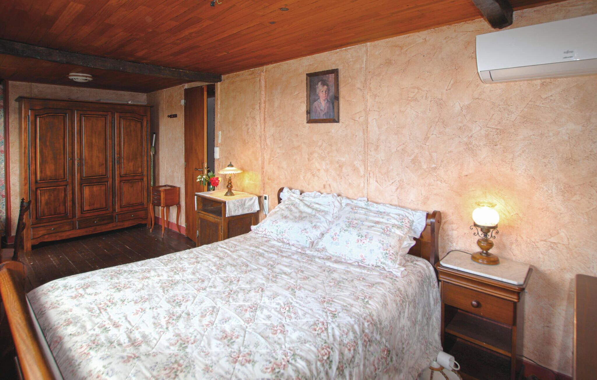 Un dormitorio con una cama de madera, una mesita de noche con lámpara, un aparador y un equipo de aire acondicionado en la pared.