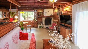 Ein gemütliches Blockhaus-Interieur mit Holzbalkendecke, Kamin, Fernseher und Essbereich.