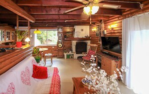 Ein gemütliches Blockhaus-Interieur mit Holzbalkendecke, Kamin, Fernseher und Essbereich.