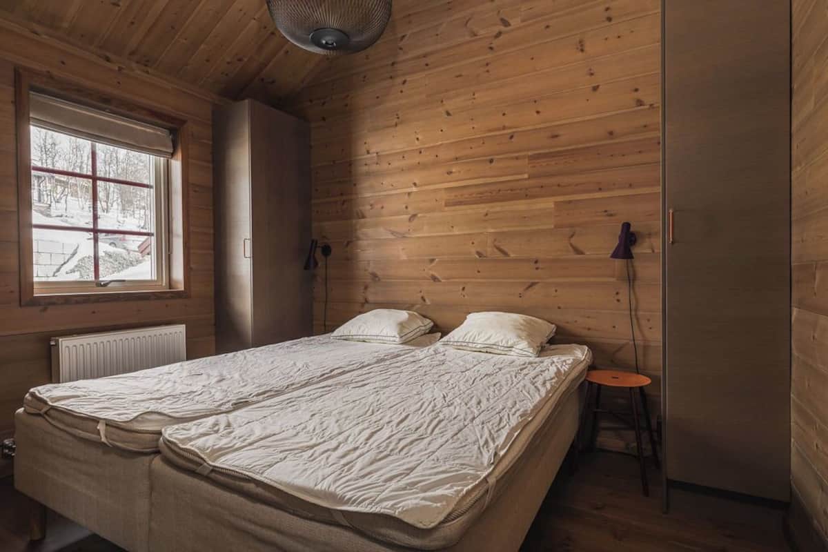 A room with two beds, a window, a radiator, and a small stool.