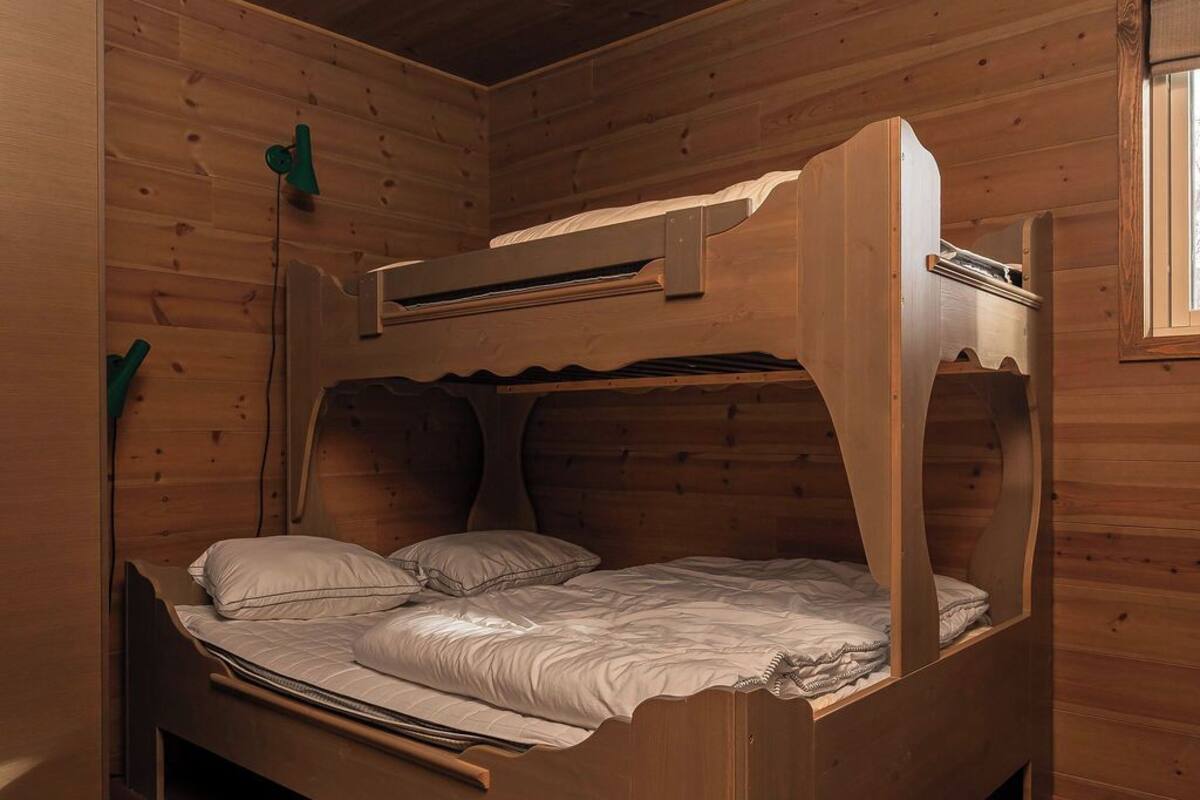 A wooden bunk bed with a headboard, a ceiling light, and a patterned rug.