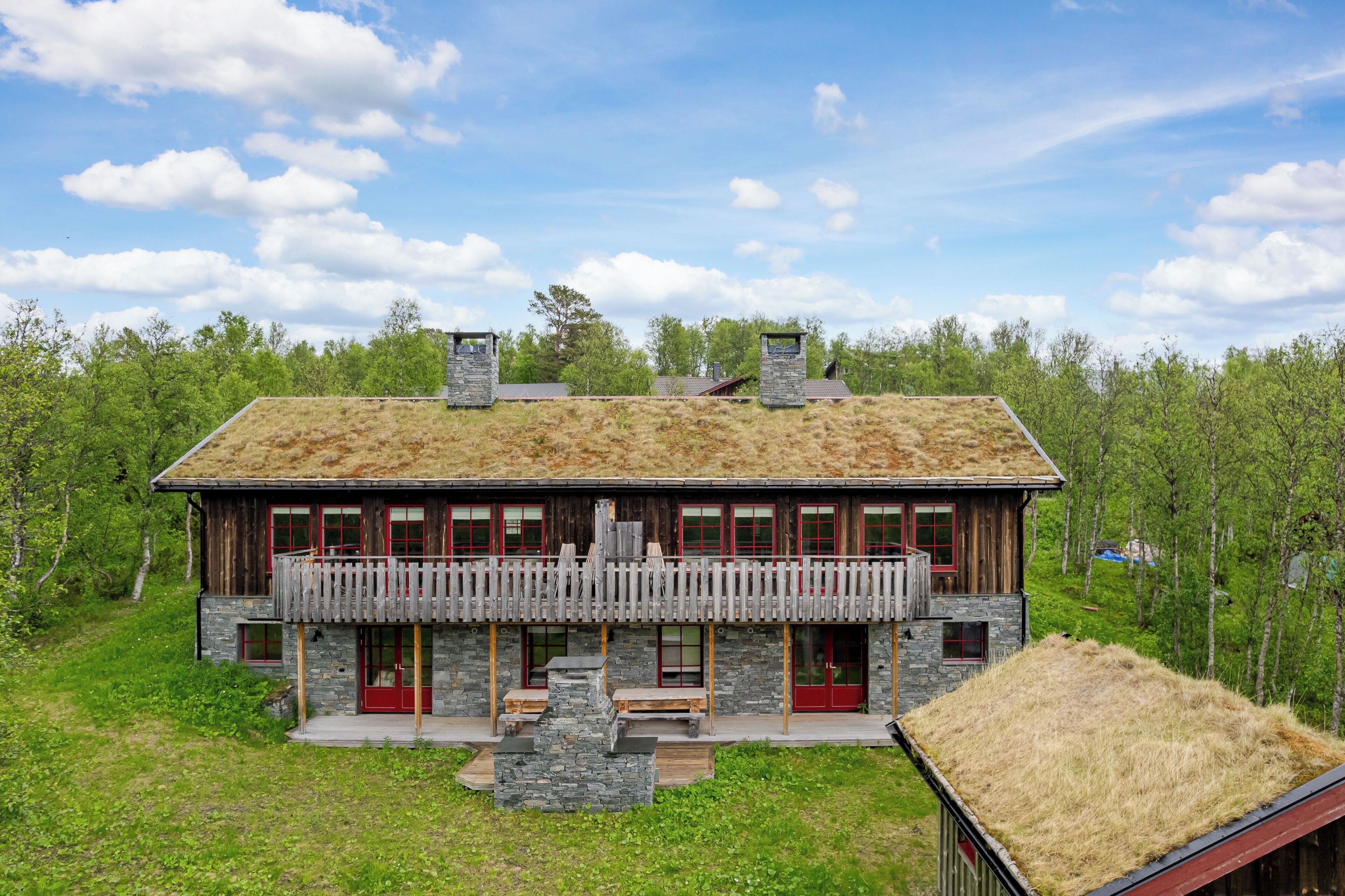 A rustic wooden house with a stone facade, a balcony, and a thatched roof.