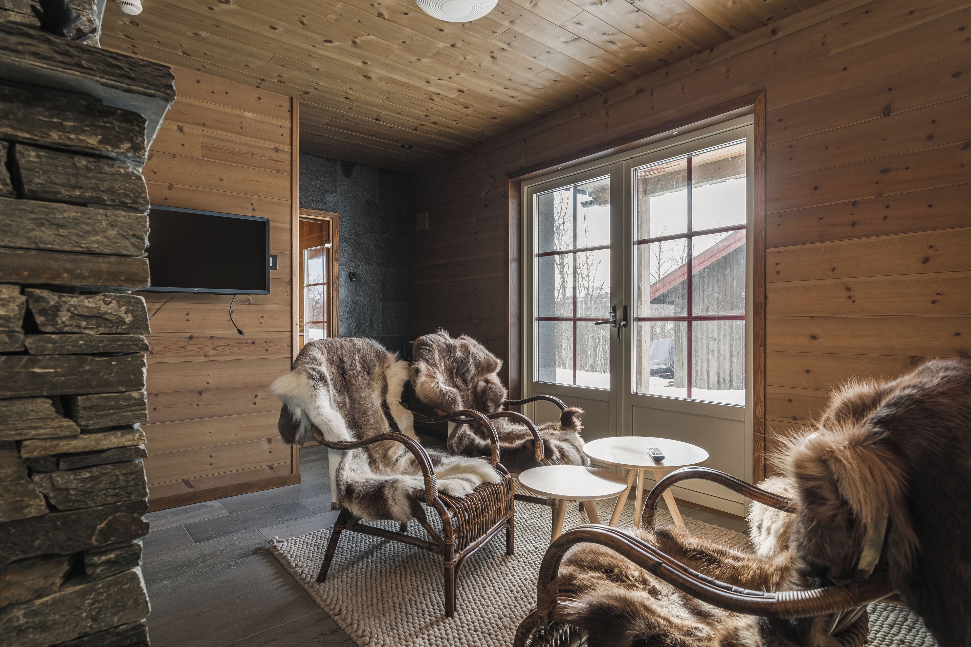 A cozy room with wooden walls and a stone accent wall, furnished with wicker chairs and a small round table.