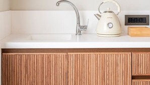 A kitchen with a white countertop, a stainless steel faucet, a kettle, and wooden cabinetry. - Volaka Luxury Suites `Ruby` (Kos)