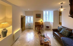 Ein Wohnzimmer mit einer Couch, einem Couchtisch, einer Lampe, einem Klavier und einem Fenster.