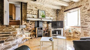 A rustic room with stone walls, a fireplace, a television, and a sofa. - Charmante maison au calme (Saint-Yrieix-la-Perche)
