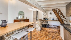 A kitchen with a stone wall, wooden beams, a tiled floor, and a wooden staircase. - Charmante maison au calme (Saint-Yrieix-la-Perche)