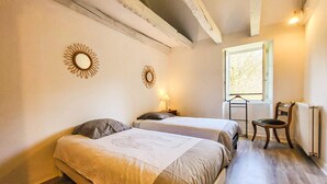A bedroom with two beds, a window, a chair, and a radiator. - Charmante maison au calme (Saint-Yrieix-la-Perche)