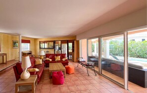 Ein großzügiger Wohnbereich mit einem roten Sofa, einem Holztisch und einer Glastür, die auf eine Terrasse im Freien führt.