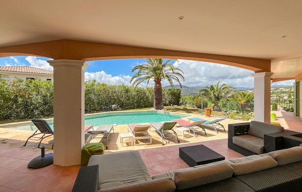 Ein überdachter Außenbereich mit Pool, Liegestühlen und einer Sitzecke.