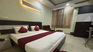 A hotel room with a large bed, a bedside table, a wardrobe, and a window with curtains. - Hotel Cityleaf (Shimoga)