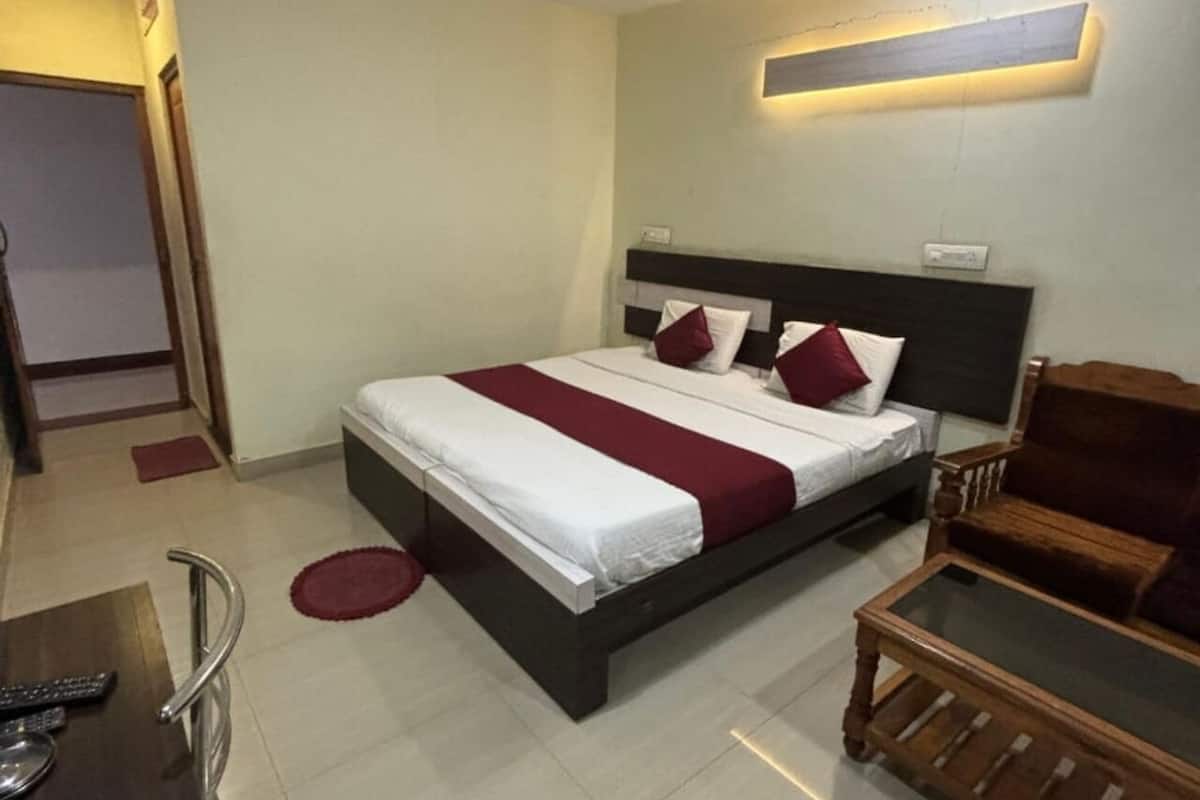 A hotel room with a bed, a wooden chair, a small table, and a remote control on a chair.