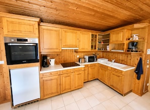 Una cucina con mobili in legno, frigorifero in acciaio inossidabile, forno, microonde e macchina del caffè.