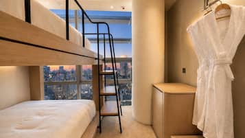 Una habitación de hotel moderna con una cama litera, un escritorio pequeño, una bata y vistas a la ciudad.