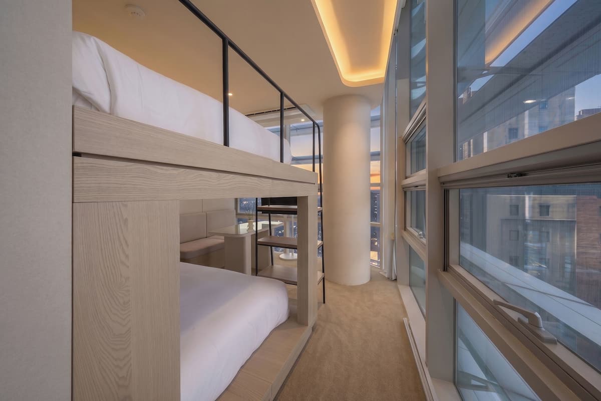 Una habitación de hotel moderna con literas, un ventanal grande y vistas a la ciudad.