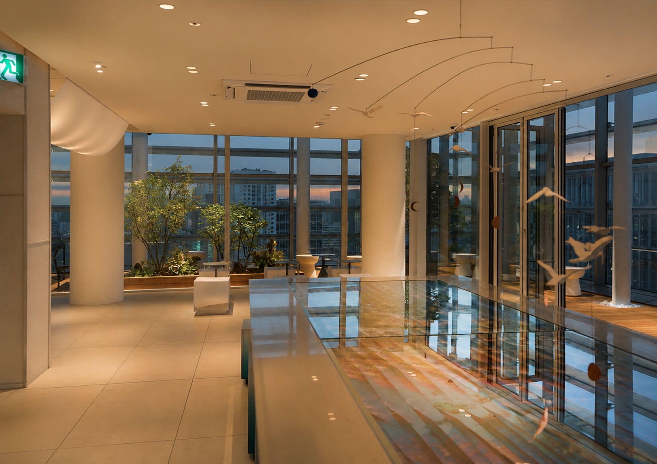 Un interior moderno con ventanas amplias, barandilla de vidrio y plantas de interior.