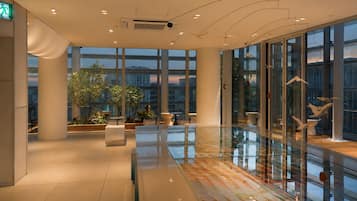 Un interior moderno con ventanas amplias, barandilla de vidrio y plantas de interior.