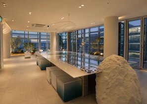 Een modern interieur met een lange, reflecterende tafel, zitplaatsen en grote ramen met uitzicht op de stad.