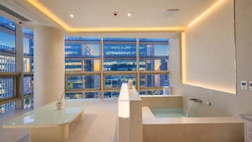 Una habitación de hotel moderna con un ventanal grande, una bañera y una mesa de vidrio.