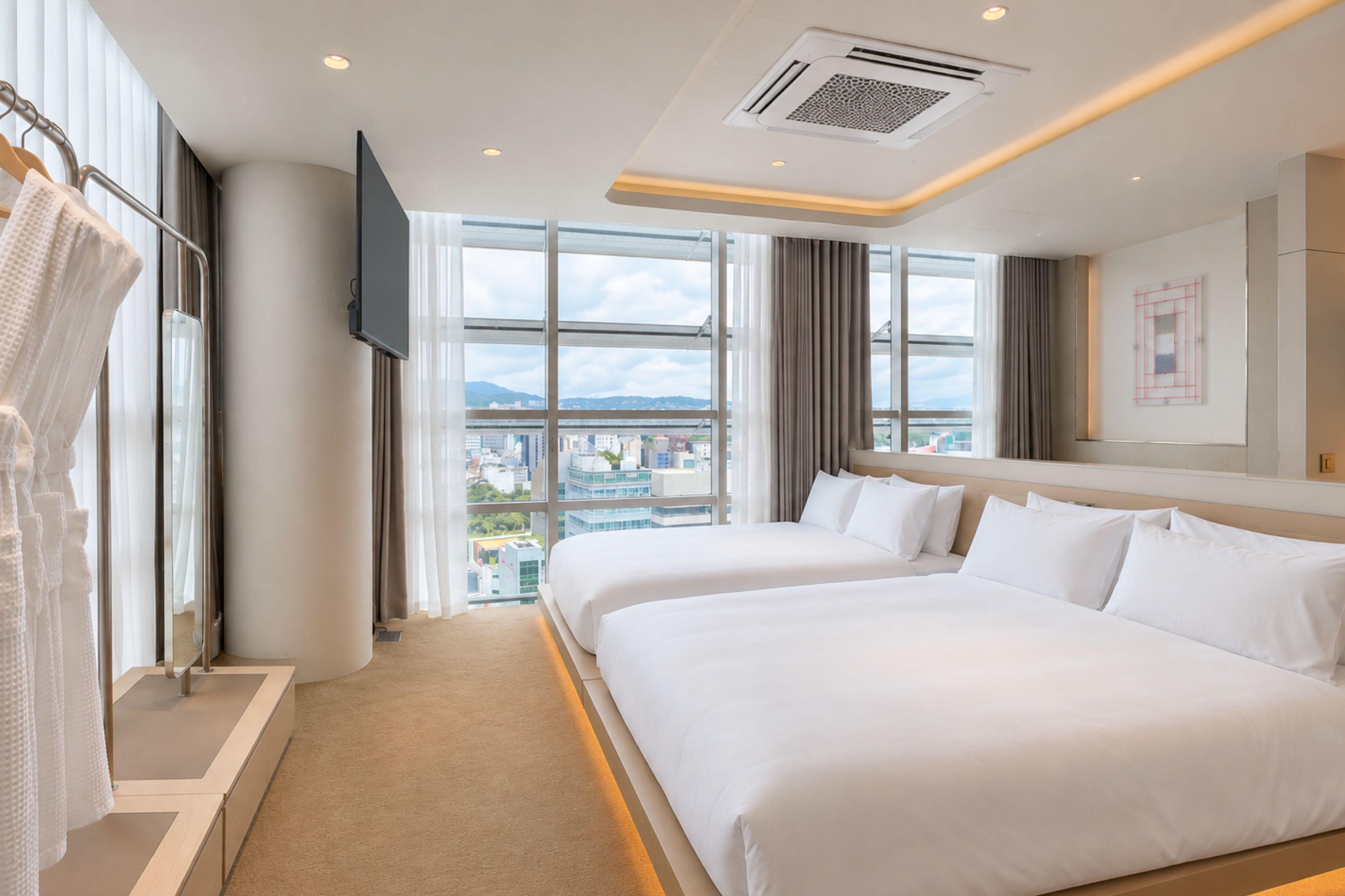 Habitación de hotel con dos camas, televisión, ventana grande con vista a la ciudad y balcón.