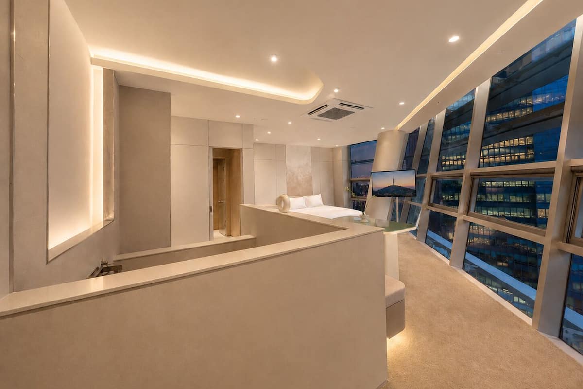 Una habitación de hotel moderna con una cama grande, un escritorio y vistas a la ciudad a través de amplios ventanales.