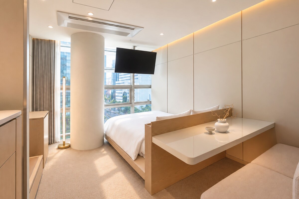 Een moderne hotelkamer met een bed, nachtkastje, televisie en uitzicht op de stad.