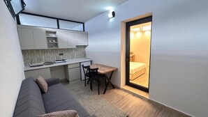 A compact living space with a sofa, a small dining table, a kitchenette, and a sliding door leading to a bedroom. - Çeşme Güzel Life (Cesme)