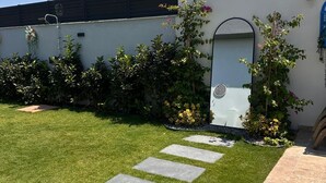 A modern building with a white facade, a glass door entrance, and a well-maintained lawn with stepping stones leading to the door. - Çeşme Güzel Life (Cesme)