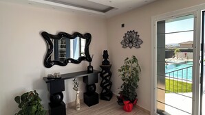 A modern living room with a large sliding glass door leading to a pool, a black console table, a mirror, and decorative wall art. - Çeşme Güzel Life (Cesme)