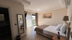 A hotel room with a bed, a bedside table with a lamp, a mirror, a painting on the wall, and a view through the window. - Çeşme Güzel Life (Cesme)