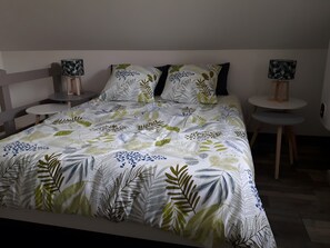 Ein Bett mit blattgemustertem Überwurf, zwei Nachttische mit Lampen und ein kleiner runder Tisch.
