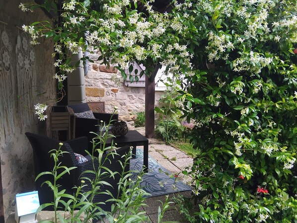 Un mur de pierres, un banc en bois et une table recouverte d’une nappe tissée.