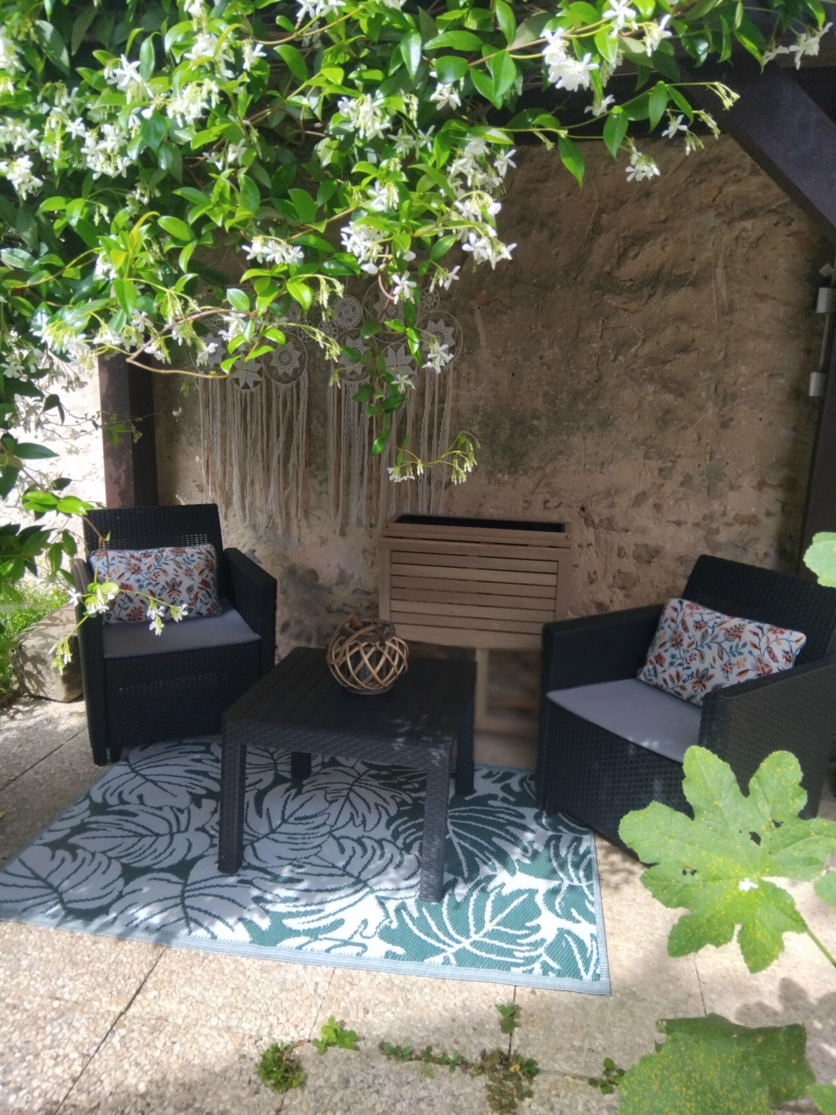 Ein Sitzbereich im Freien mit Korbmöbeln, einem gemusterten Teppich und einer Wandverziierung.